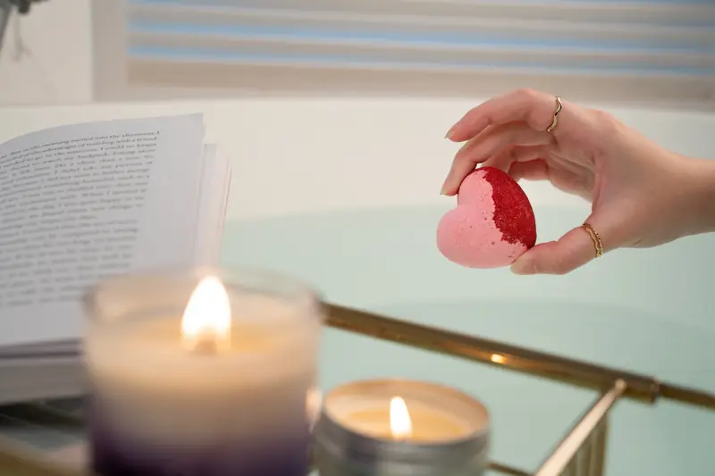 Hand holding a bath bomb beside a lit candle