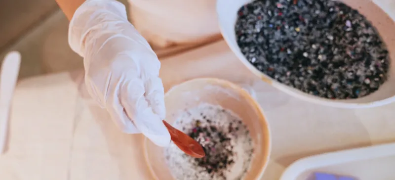 Gloved hand mixing recycled phone-case granules into a white composite