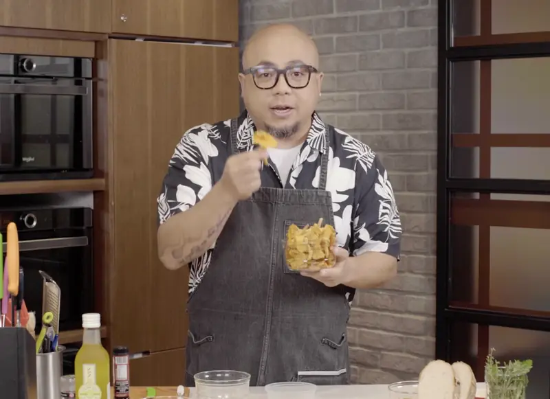 Chef in an apron presenting a dish in a home kitchen