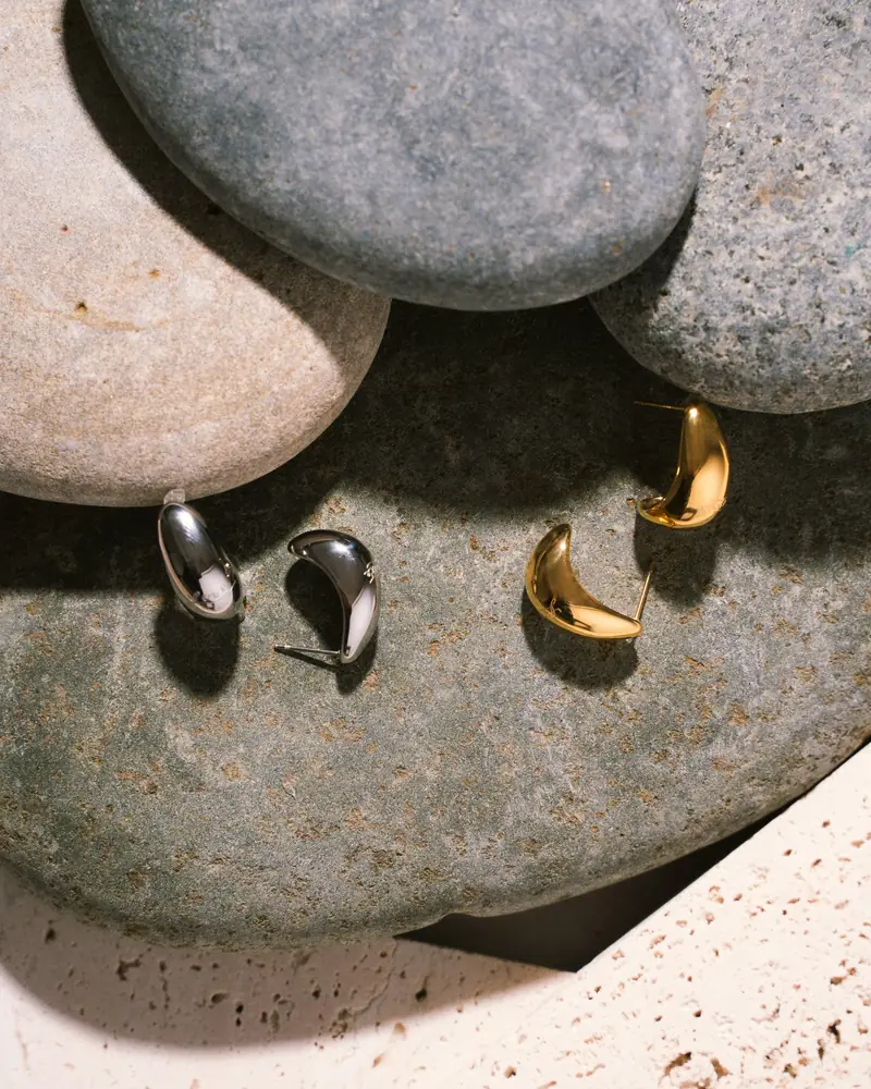 Gold and silver earrings resting on smooth grey stones