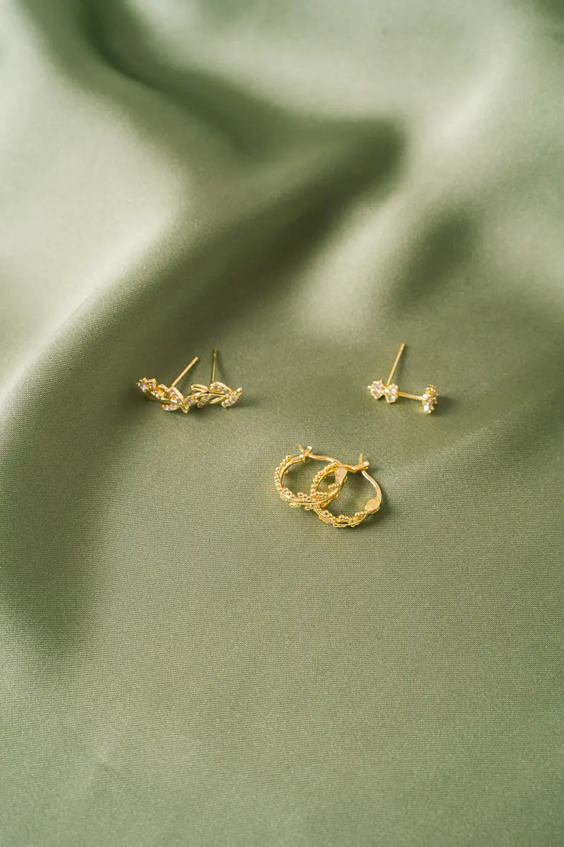 Gold earrings on sage-green fabric