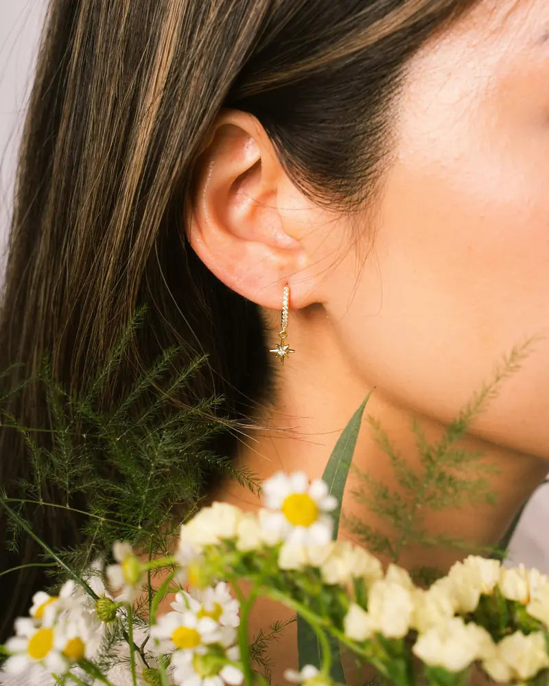 Profile of a model wearing an earring beside yellow flowers