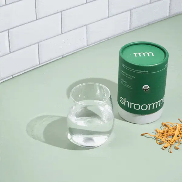 Green Shroommate canister beside a glass of water