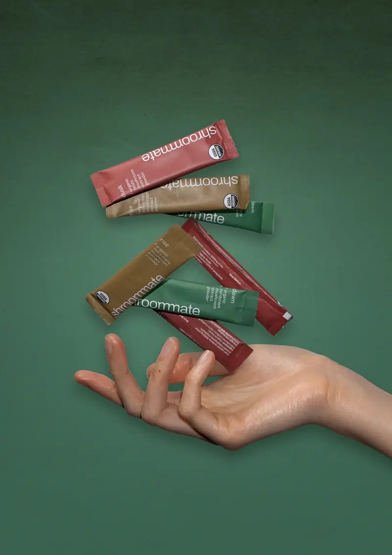 Hand holding Shroommate sachets on a green background