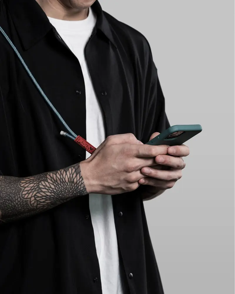 Model in black using a phone on a strap