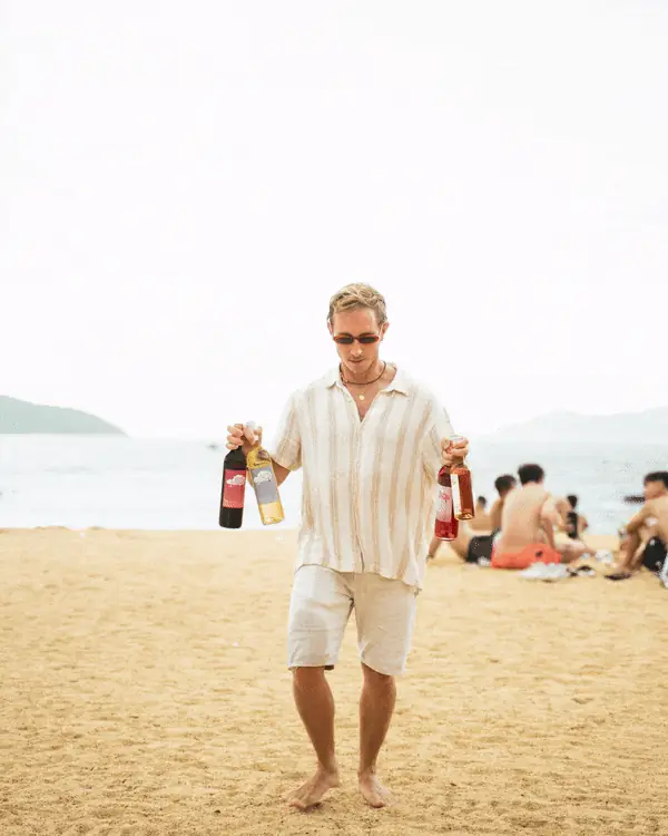 Man walking along a beach holding a bottle